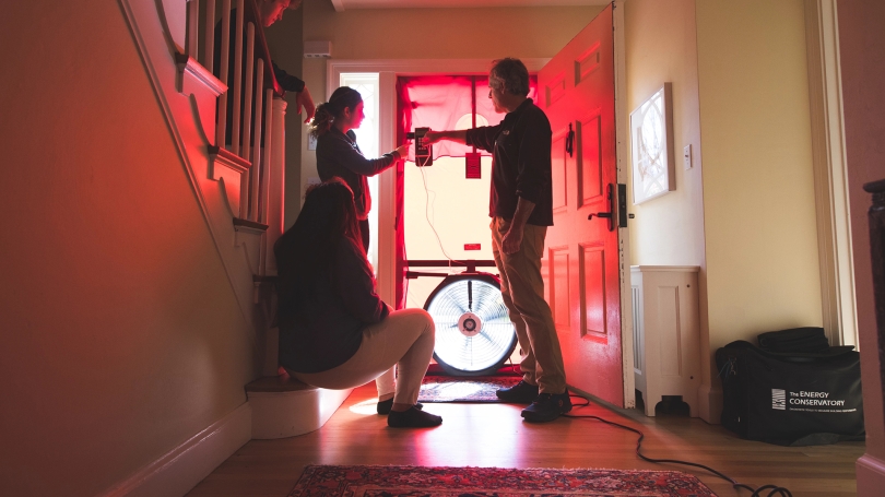 A photo of students looking at the meter on a vacuum sealed door applied during an energy audit of Montgomery House